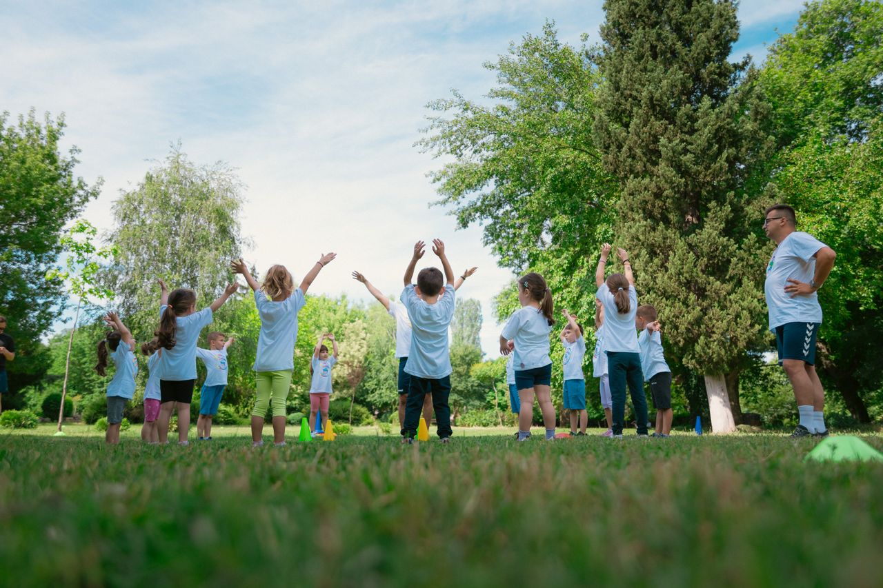 Group of children with instructor doing exercises in a sunny park setting, promoting outdoor activity.