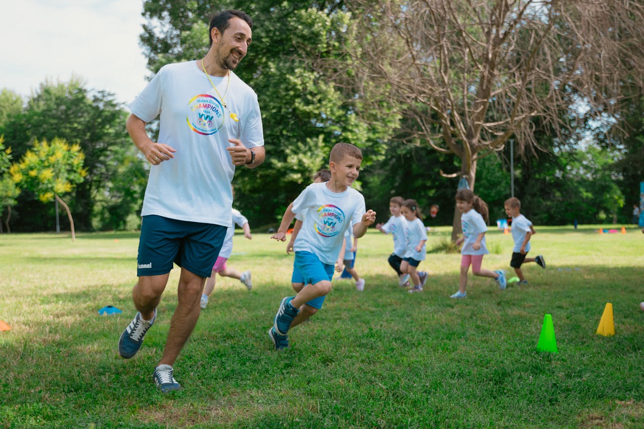 A group of kids running with an instructor during outdoor sports activities on a sunny day in a park.