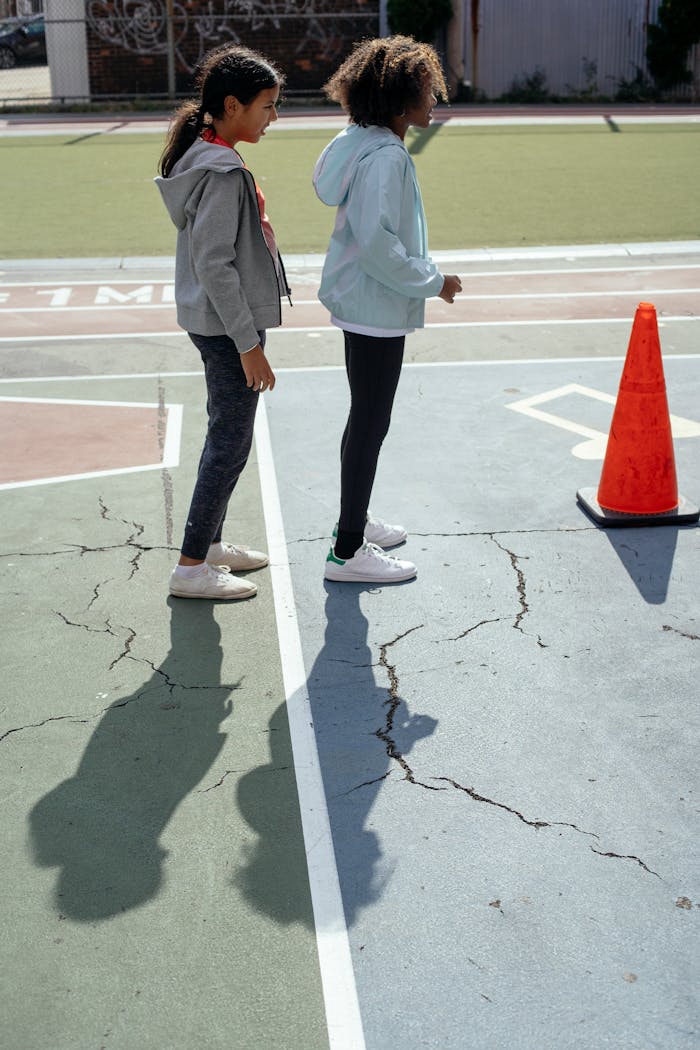Side view of multiracial girls in similar sportswear playing together in active games on playground located in backyard of school on sunny day